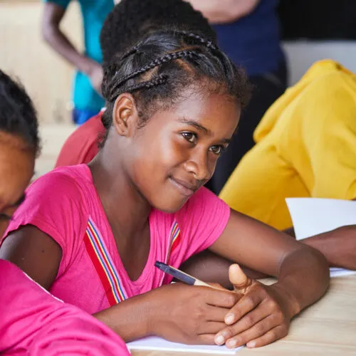 Jeune fille malgache écrivant à une table lors d’une activité éducative.