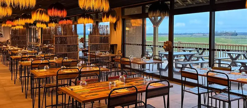 Salle de restaurant chaleureuse avec tables dressées et vue sur la terrasse extérieure.